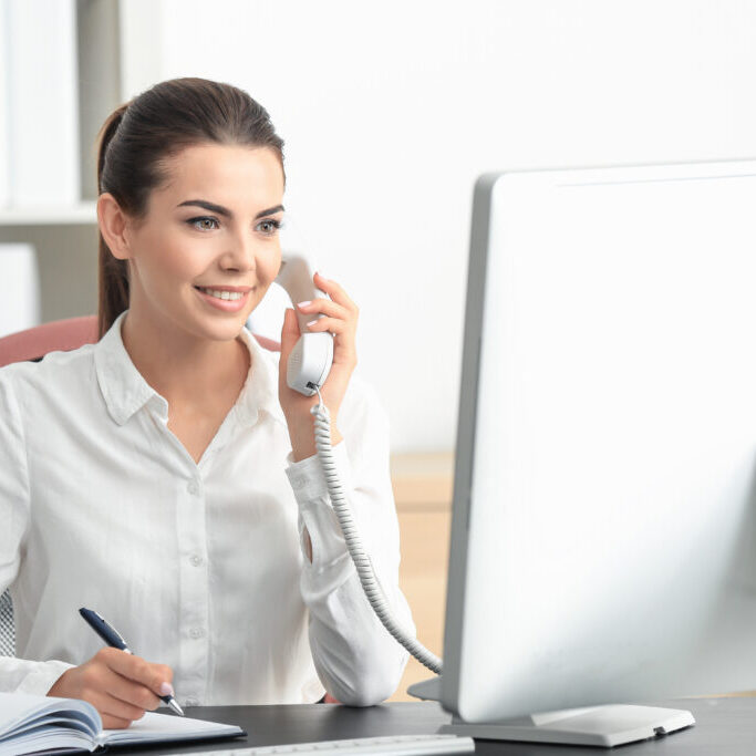 Young female receptionist talking on phone in office